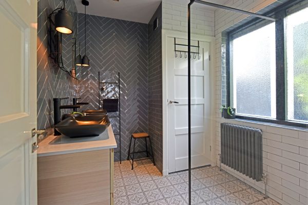 Badkamer met keramische patroontegel, grijze visgraat tegels op de wand, en paneeldeur